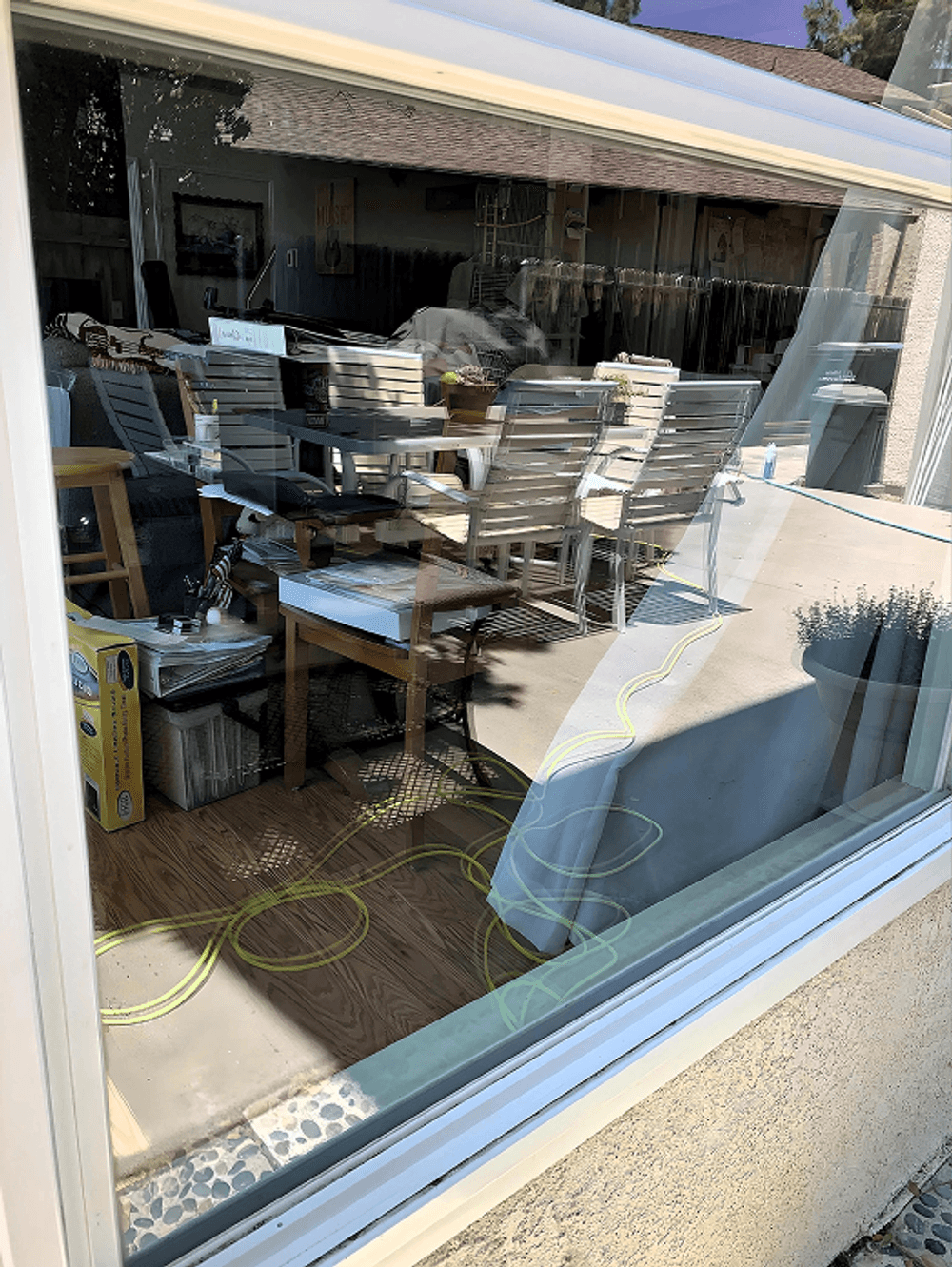 Reflection in window showing a dining area with chairs, a table, and cluttered items inside.