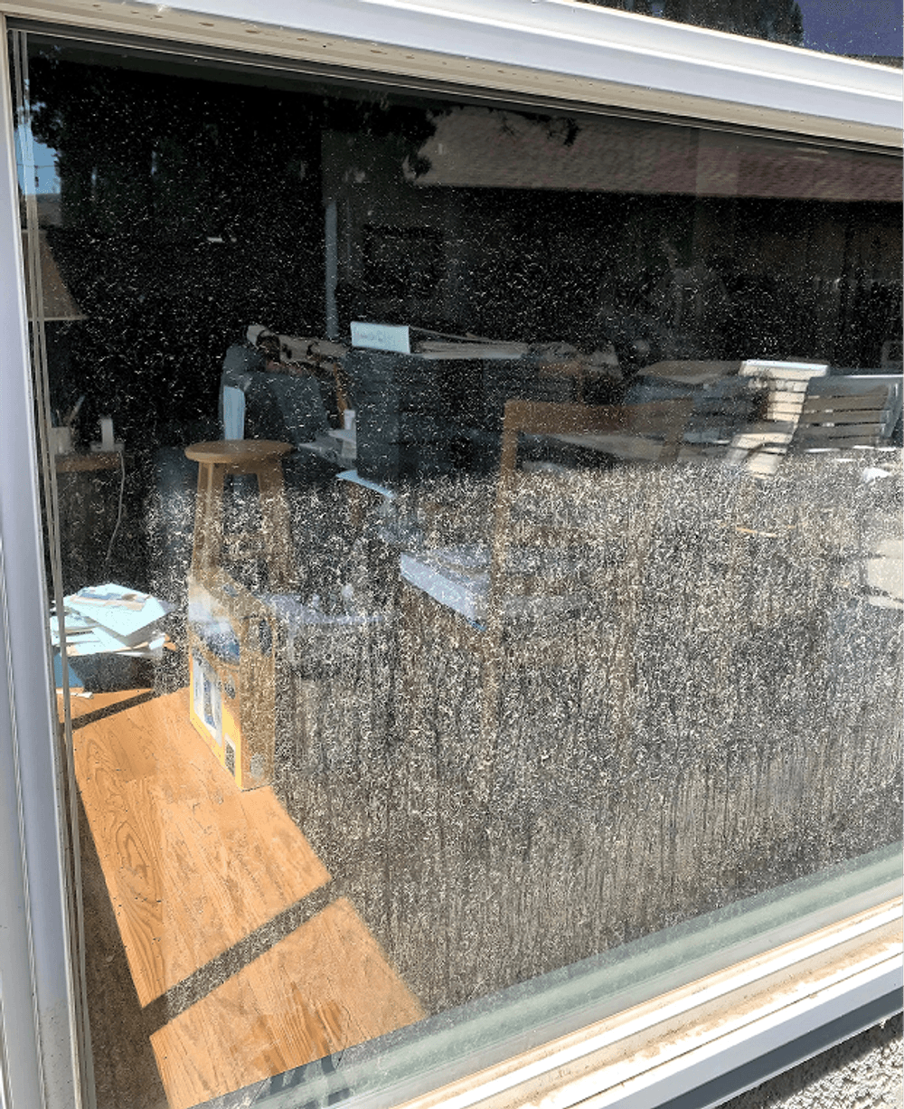 Dirty window reflecting furniture and clutter in a sunlit room.