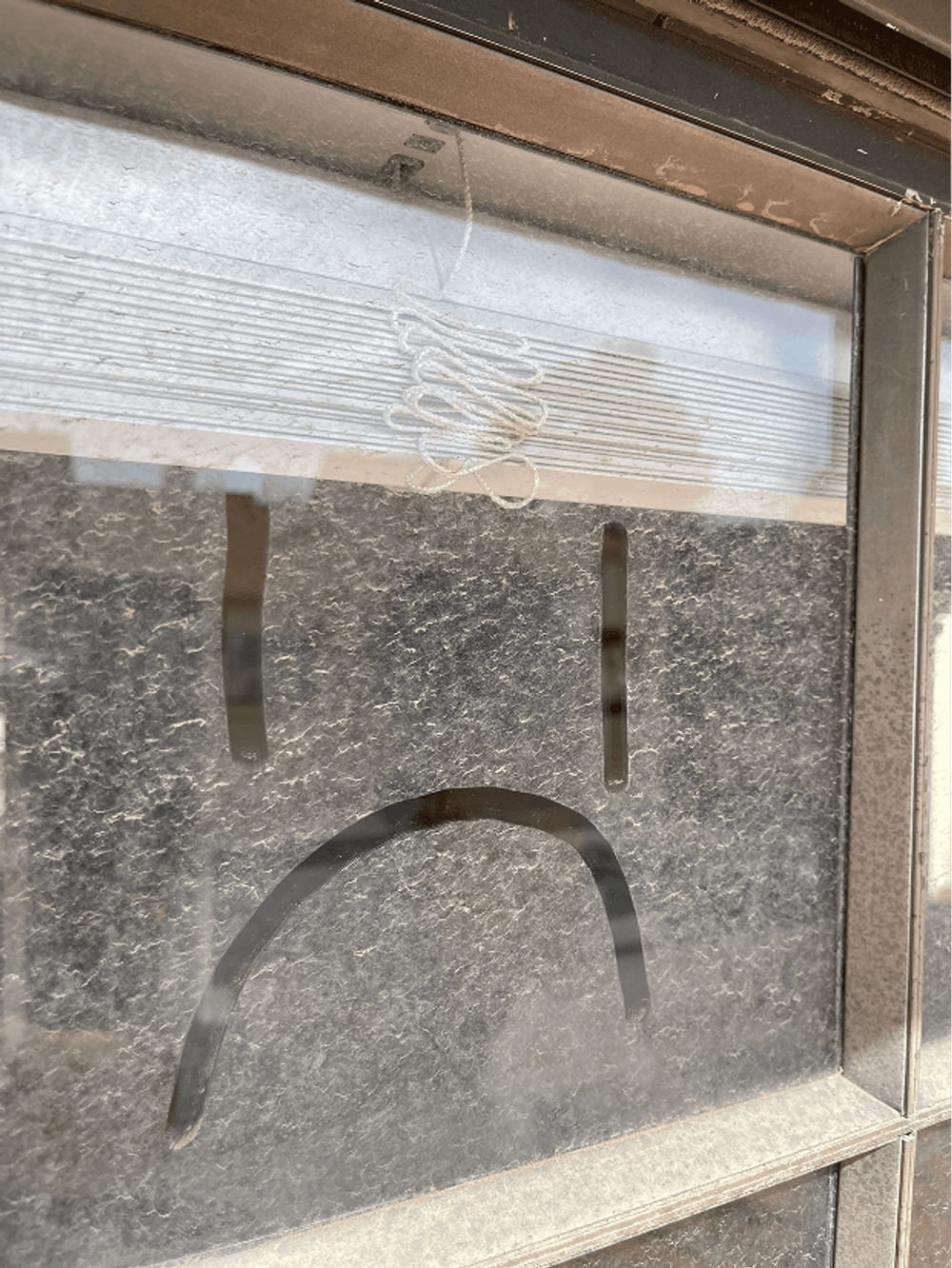 Window with sad face drawn in condensation, highlighting feelings of loneliness or sadness.
